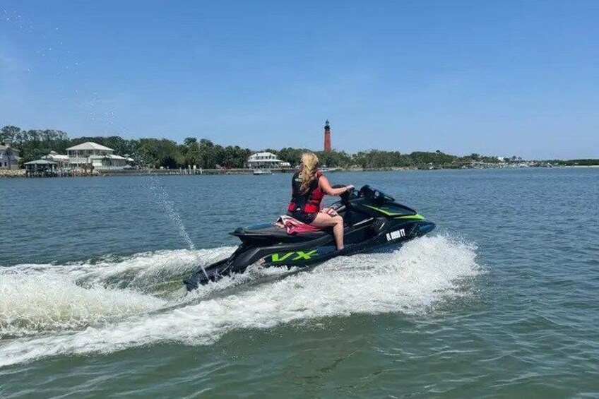 A person riding a jet ski on a body of water with a lighthouse in the background. 1