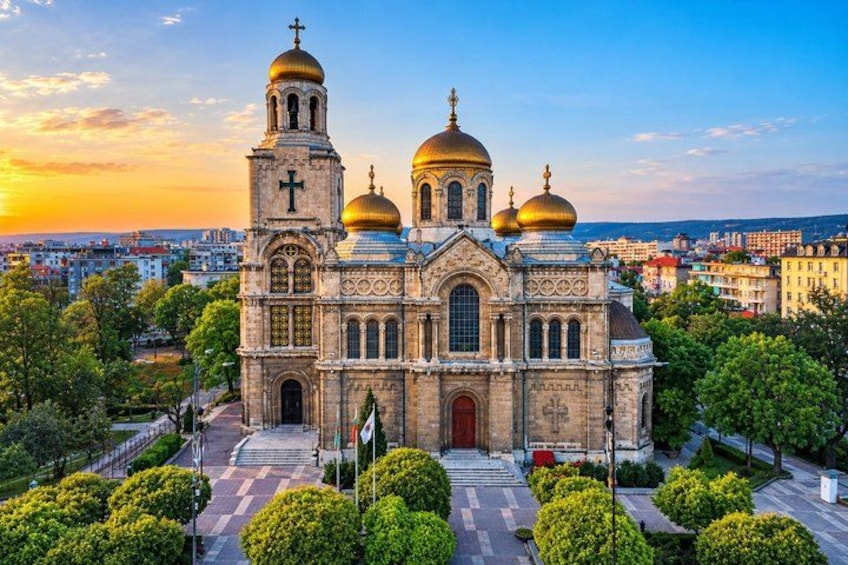A historic church with multiple domes and a bell tower, surrounded by greenery and urban buildings. 1