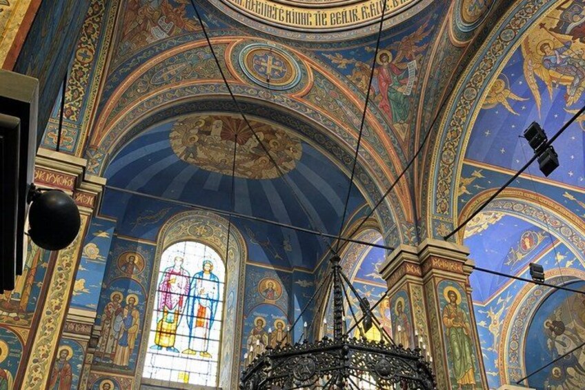 A church interior with ornate ceiling frescoes, a stained glass window, and a chandelier. 2