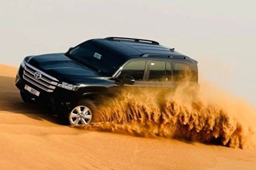 A black SUV driving through a sandy desert, kicking up a large cloud of sand. 1