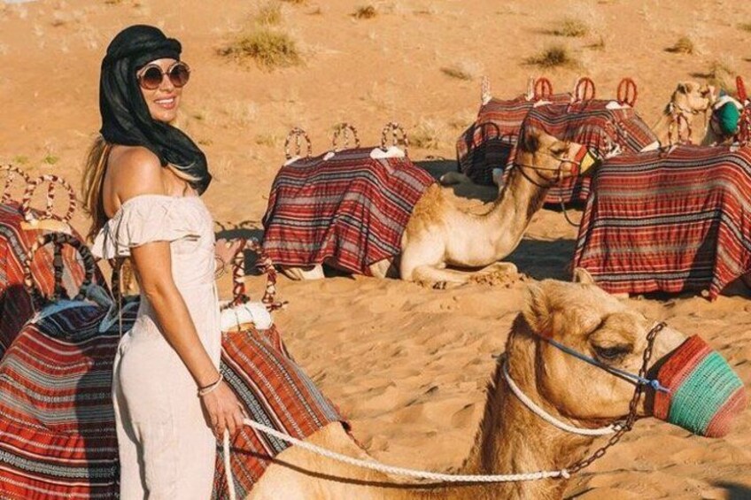 A person riding a camel in a desert with camels and colorful blankets. 5