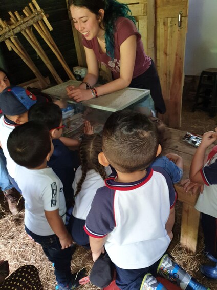A woman interacting with children in a rustic setting with wooden structures and hay on the ground. 4
