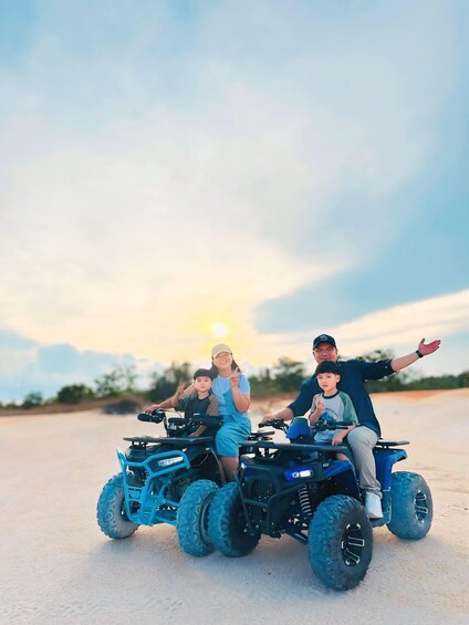 Drei Personen fahren mit Quads auf einer unbefestigten Straße, im Hintergrund ein Sonnenuntergang. 5