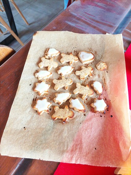 A wooden table with a piece of parchment paper on it, holding several cookies shaped like animals. 3