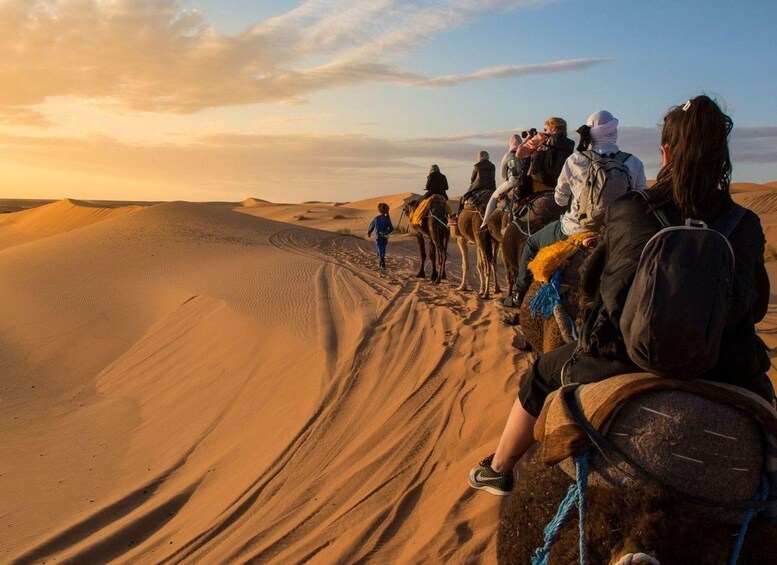 Un grupo de personas montando camellos a través de un paisaje desértico al atardecer. 2