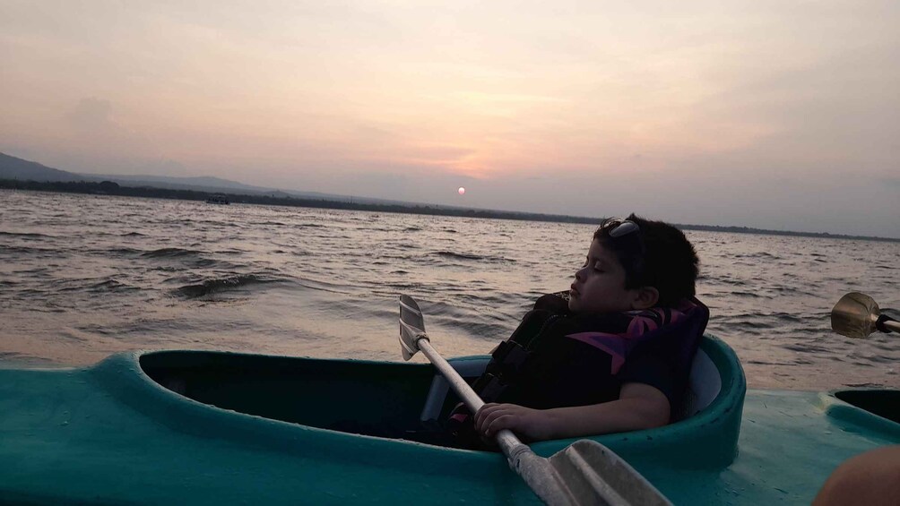 Una persona en un cayuco verde sobre un cuerpo de agua al atardecer. 2