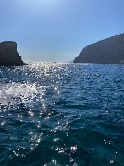 Mar tranquila con aguas azul cristalino reflejando la luz del sol, rodeada de acantilados rocosos bajo un cielo despejado. 3