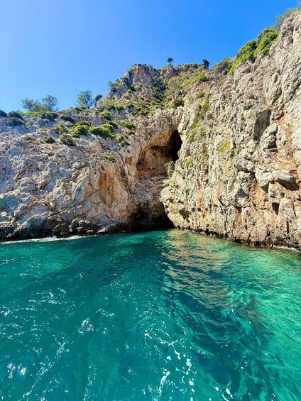Costa rocosa con mar azul cristalino, entrada a una cueva y vegetación escasa en los acantilados. 5