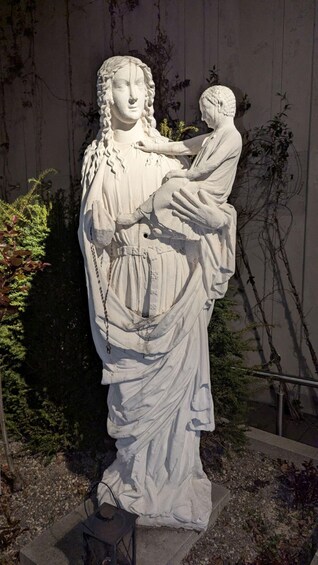 A statue of a woman holding a child, set against a wall with climbing plants. 3