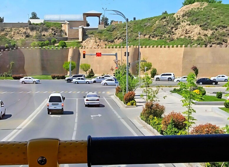 A multi-lane road with vehicles, traffic lights, and a hill with buildings in the background. 2