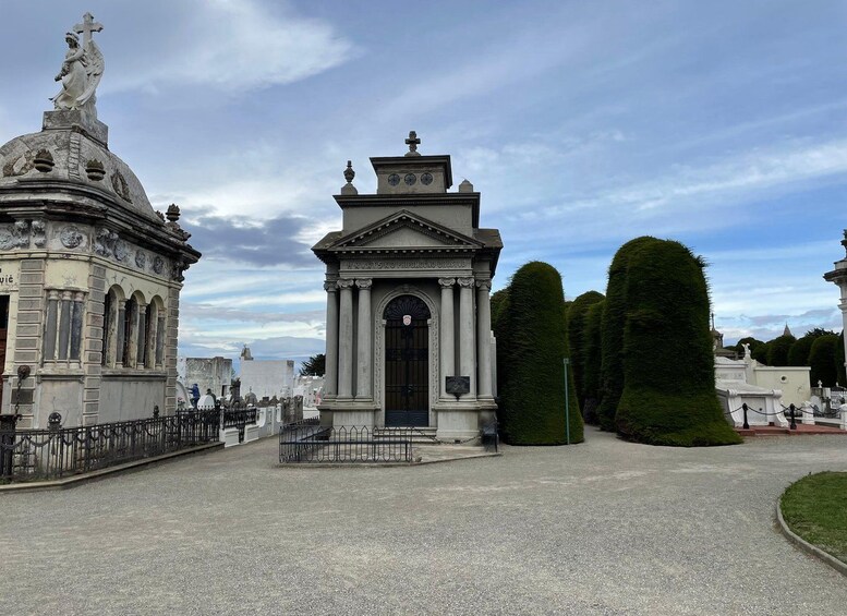 Un cementerio con un monumento central, una estatua y setos bien cuidados. 2