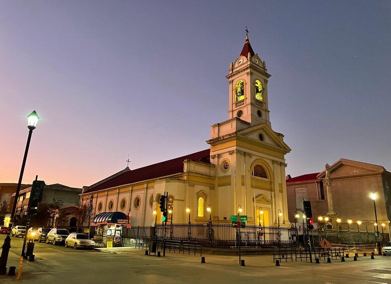 Una iglesia con una torre de reloj, faroles de la calle y coches aparcados. 5