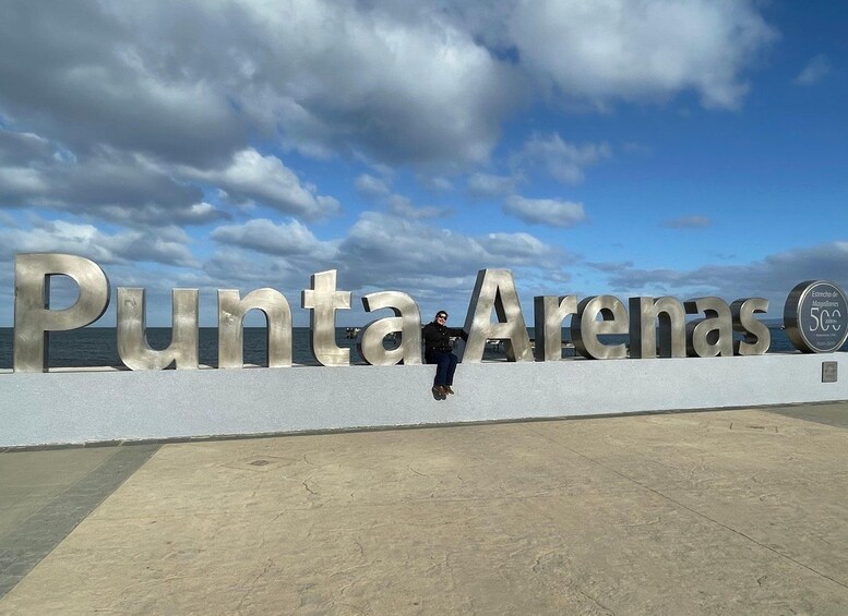 Un letrero grande con las palabras 'Punta Arenas' y una persona sentada encima. 1