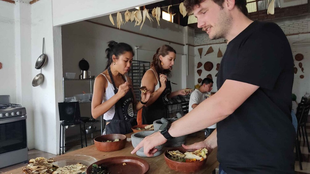 A kitchen with people preparing food, a stove, and various cooking utensils. 5