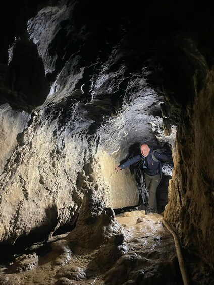 A person exploring a cave with rough, uneven walls and a narrow passageway. 1