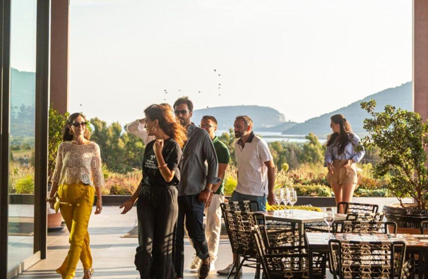 A group of people walking outdoors, a table with chairs, and a scenic view of hills and water in the background. 1
