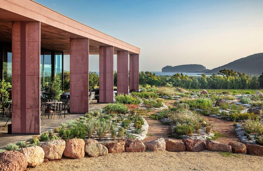 A modern building with large columns, outdoor seating, and a landscaped garden with rocks and plants. 4