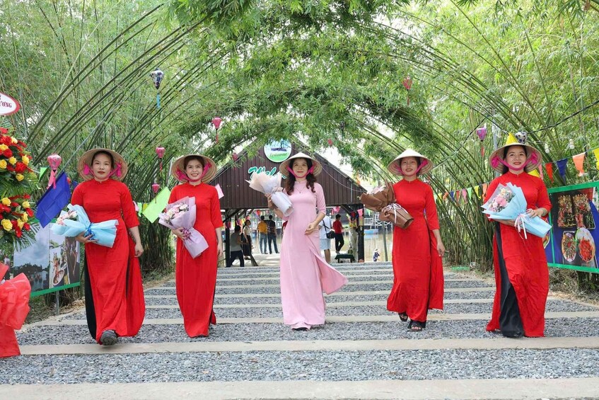A group of women in red dresses and conical hats walking through a bamboo archway. 2