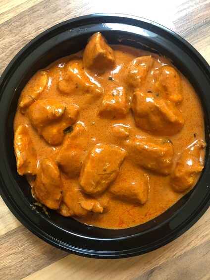 A black bowl containing a creamy orange curry with chunks of chicken. 2