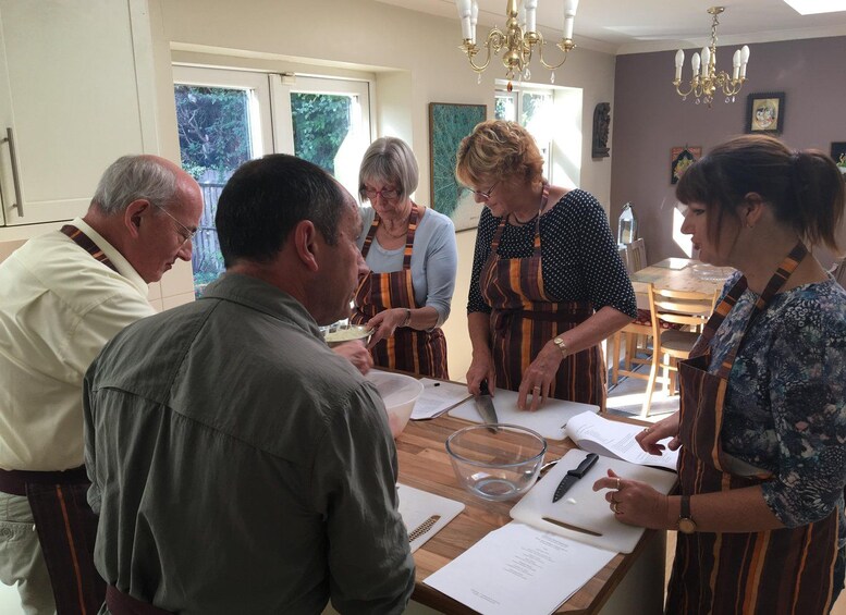 A group of people in a kitchen preparing food, with a cutting board, knife, and papers on the table. 3