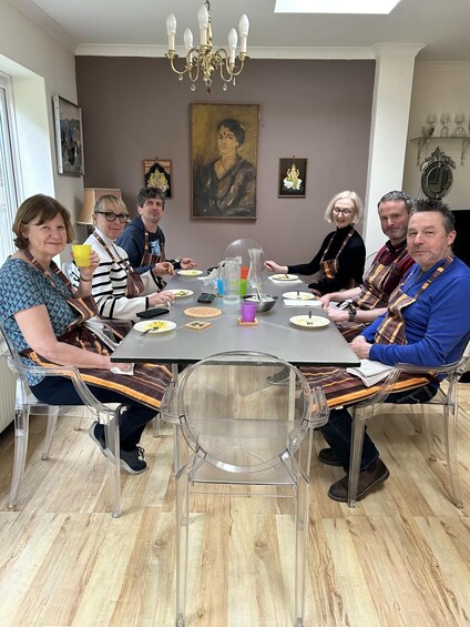 A group of people sitting around a table with food, in a room with a chandelier and paintings on the wall. 1