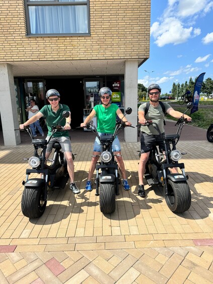 Tres personas en patinetes eléctricos frente a un edificio con un letrero que dice 'E-bikes'. 2