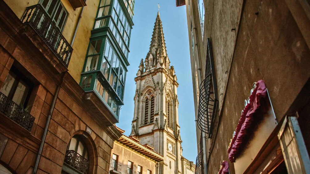 A narrow street with a tall church spire, adjacent buildings, and a metal gate. 3