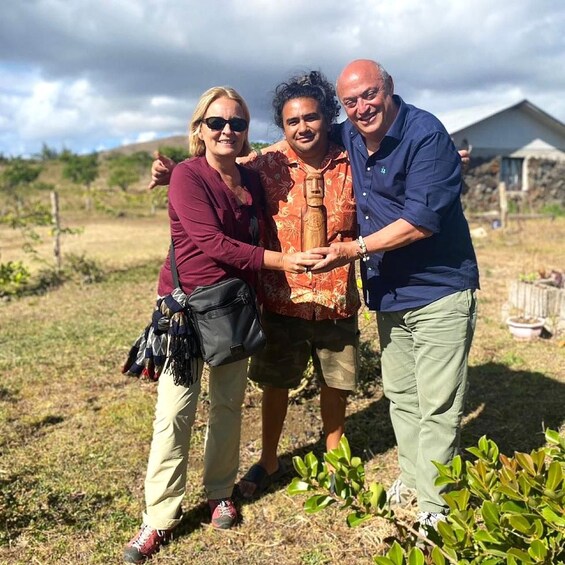 Three people outdoors with a house and greenery in the background. 2