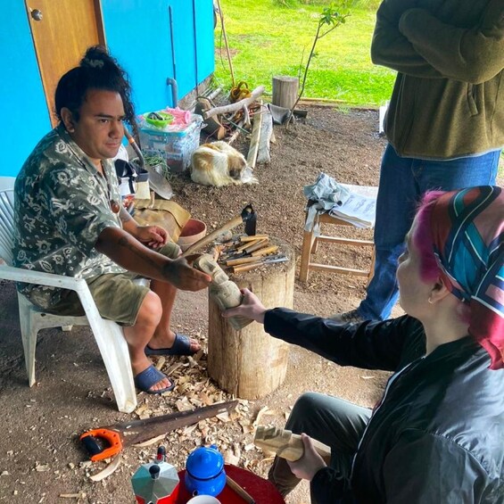 A person carving a wooden object outdoors with tools and wood shavings scattered around. 1