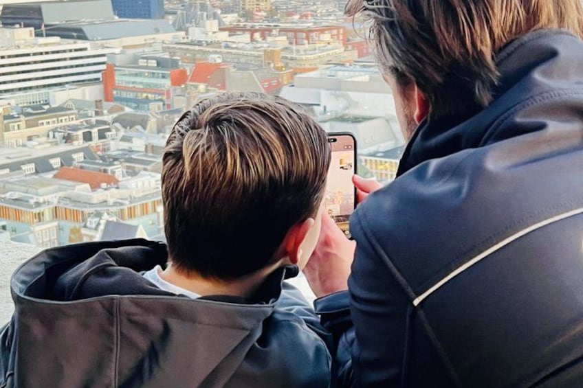 A person taking a photo of a cityscape with buildings and a bridge. 2
