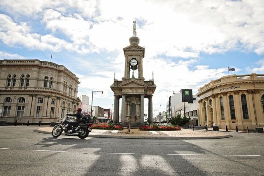 A street with a central monument, buildings, and a motorcycle. 1