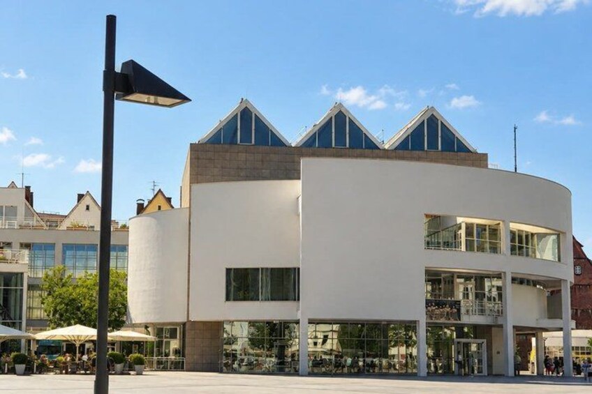 A modern building with a curved facade, large windows, and a distinctive triangular roof design. 3
