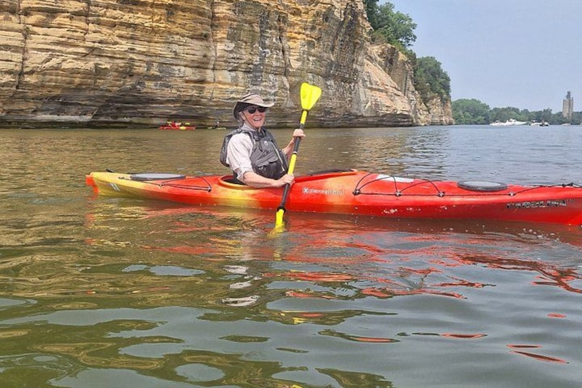 A person in a red kayak on calm water with a rocky cliff in the background. 2