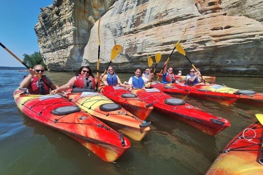 A group of people kayaking on a calm river with rocky cliffs in the background. 3