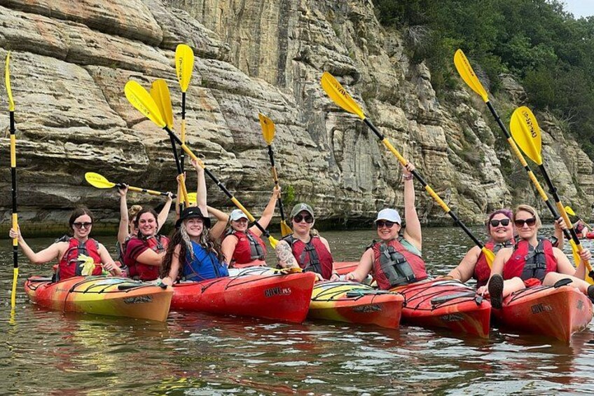 A group of people kayaking on a river with rocky cliffs in the background. 1