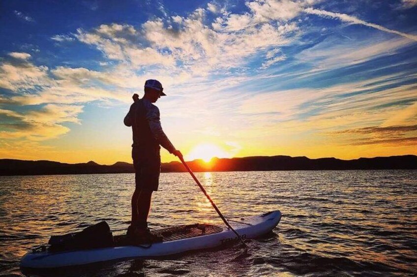 A person paddleboarding on calm water during sunset. 1