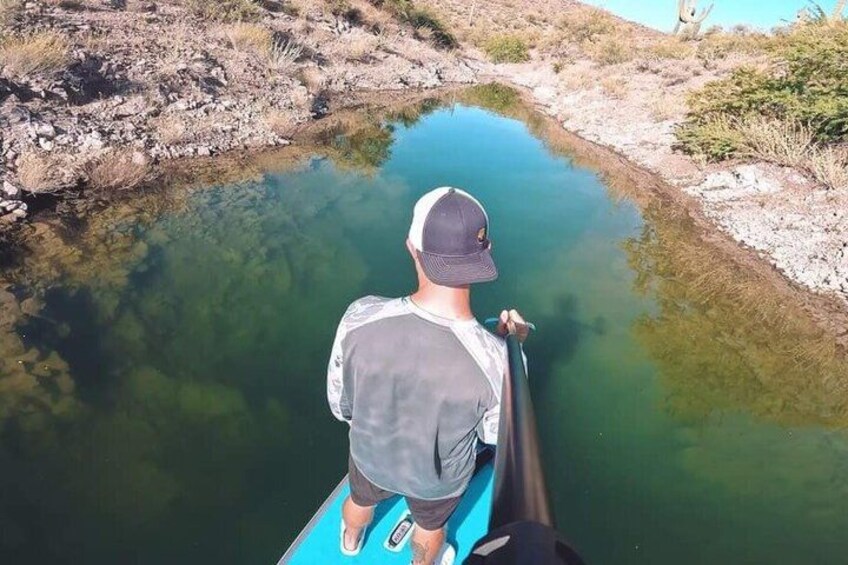 A person paddling a kayak on a calm river surrounded by rocky terrain and sparse vegetation. 4