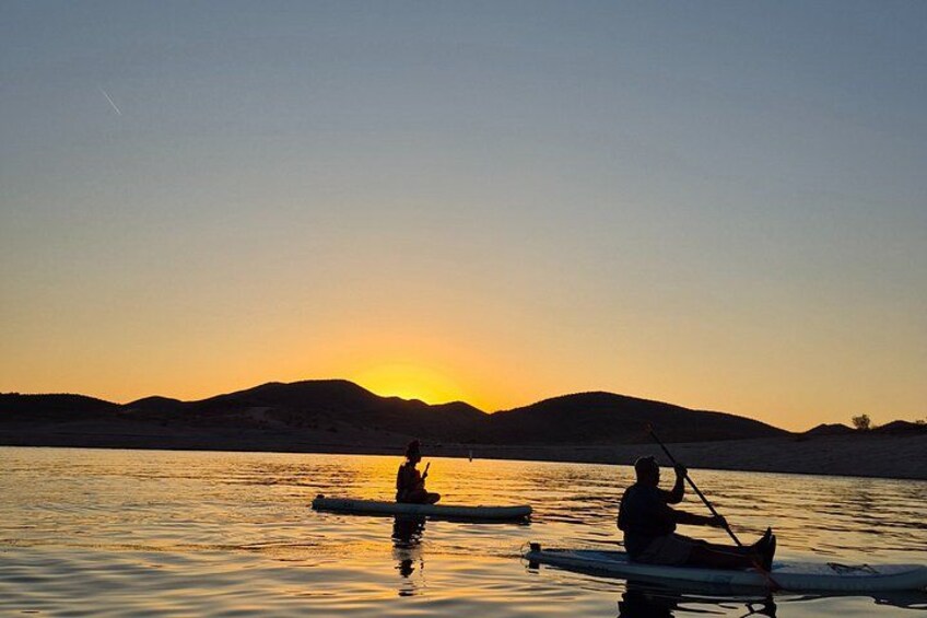 Two people kayaking on a calm body of water during sunset with a mountain range in the background. 3