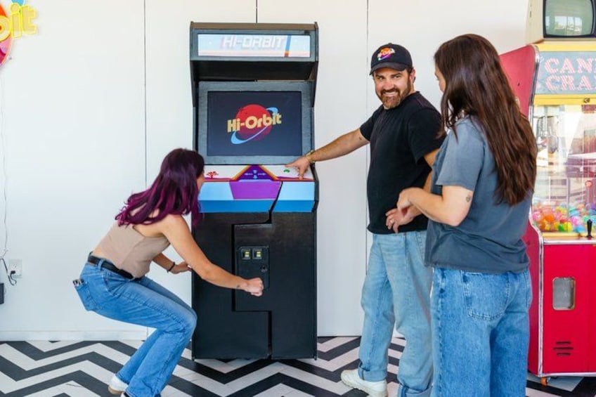 A Hi-Orbit arcade game, a red vending machine, and a black and white patterned floor. 5