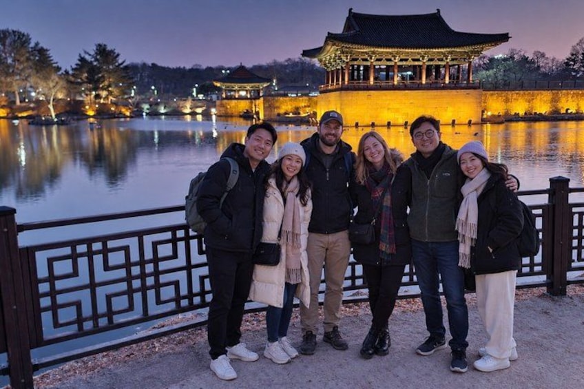 A group of people standing by a lake with a traditional building in the background. 1