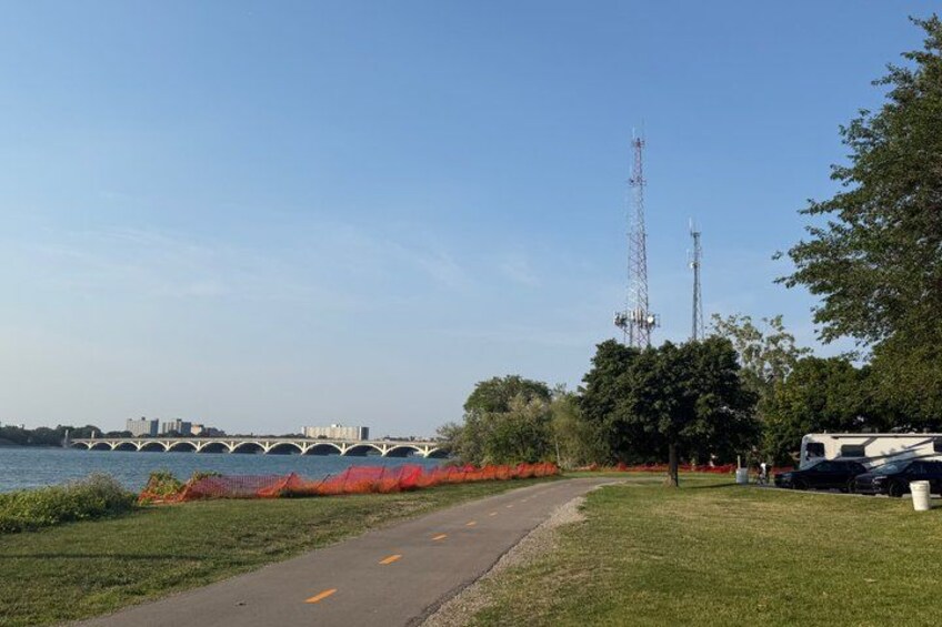 A pathway beside a river with a bridge in the background, a grassy area, and a parked RV. 5
