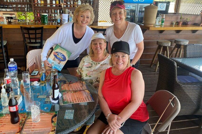A group of people at an outdoor bar with a table, bottles, and a grill. 4