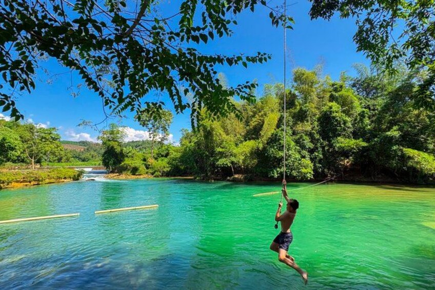 A person swinging on a rope over a clear blue water body surrounded by lush greenery. 3