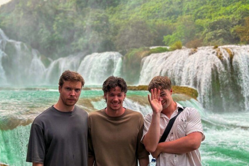 Three people standing in front of a waterfall with lush greenery in the background. 4