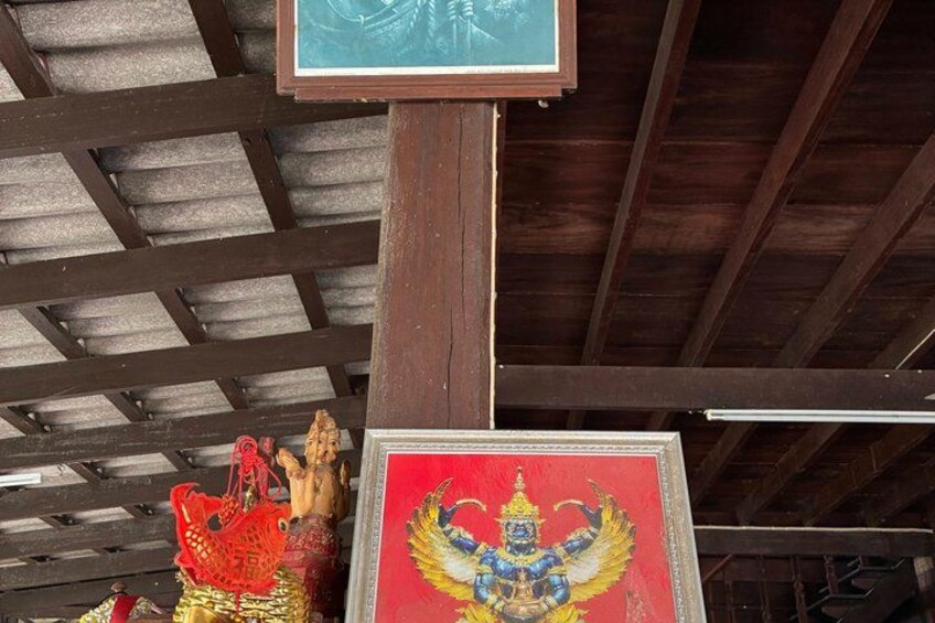 A wooden structure with a metal roof, a framed picture of a deity, and a red and gold statue. 2