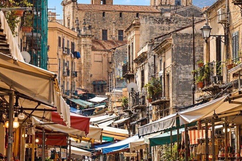 A narrow street with buildings, outdoor seating, and market stalls. 5