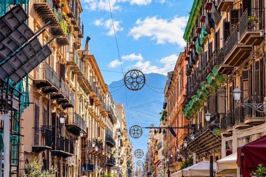 A street lined with multi-story buildings, balconies, and hanging plants. 3