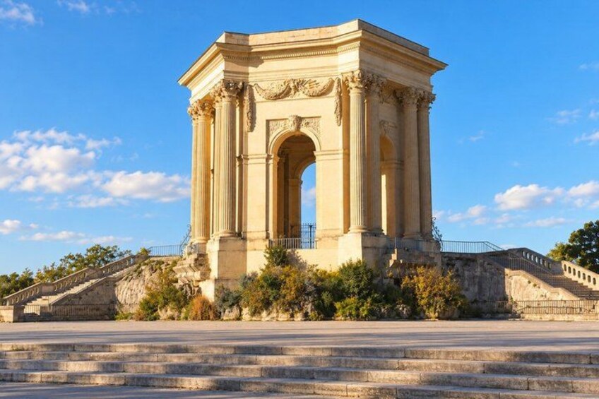 A classical monument with columns and an arch, surrounded by a stone staircase and greenery. 4