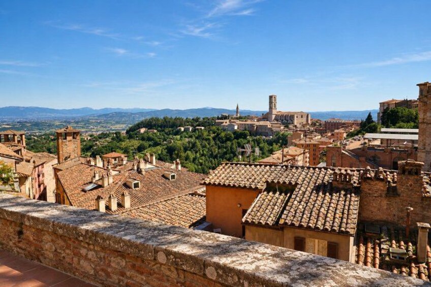 A historic town with terracotta-roofed buildings, a prominent church tower, and a mountainous backdrop. 3