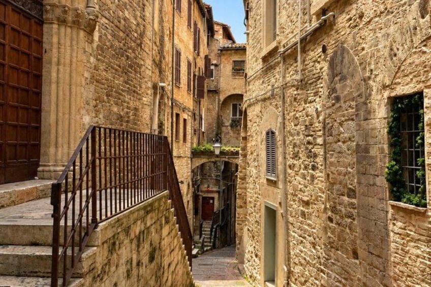A narrow stone alleyway with a wooden staircase and buildings with arched windows and doors. 5